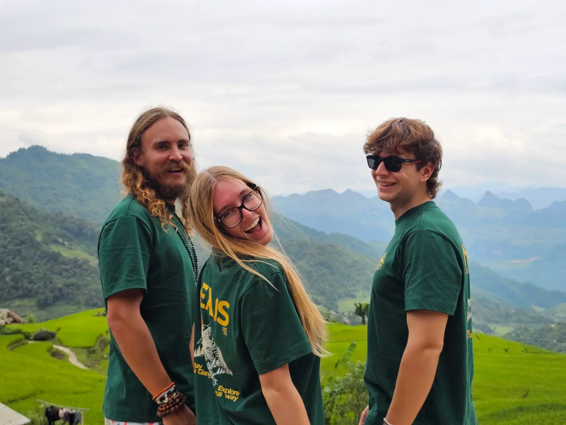 Three travellers wearing Nexus shirts with green rice terraces and Ha Giang mountains behind them